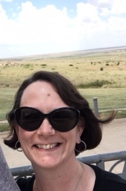 a white woman wearing sunglasses smiling at the camera on a sunny day