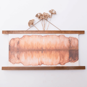 a chromatogram where the top and bottom mirror each other in hazy tans and browns. The print is hung with wooden poster bars at the top and bottom of the print. Dried flowers extend from the top of the frame.